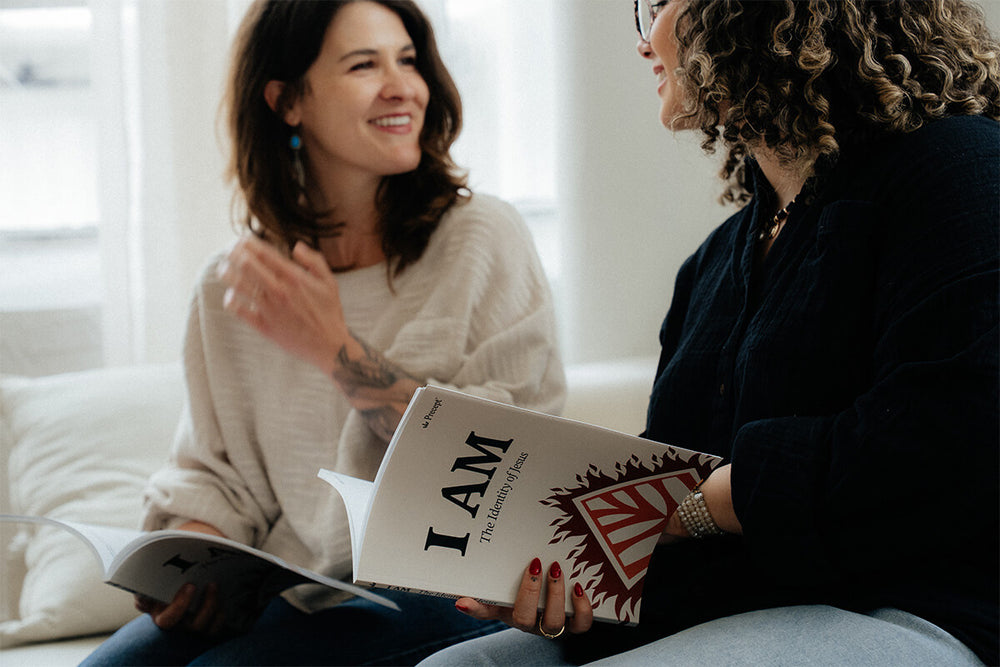 Two women sitting on a couch, one holding a book titled 'I AM: The Identity of Jesus'