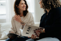 Two women sitting on a couch, one holding a book titled 'I AM: The Identity of Jesus'