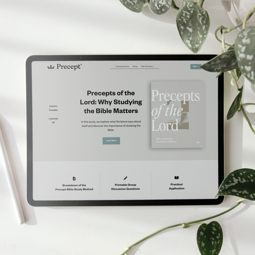 A tablet on a white surface displaying the Precept website, surrounded by green plant leaves and a white pen.